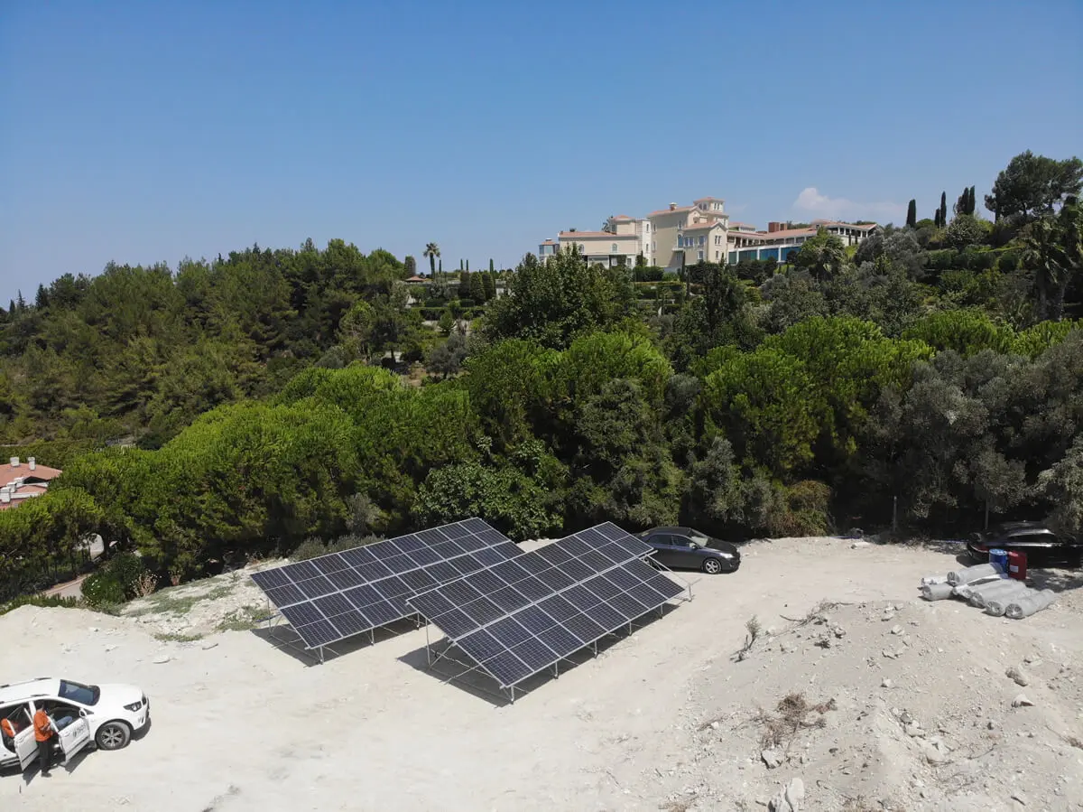 A ground-mounted solar array on open land in front of a wooded hillside